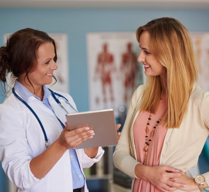 Doctor showing a tablet to a smiling patient in a clinic setting, discussing medical information.